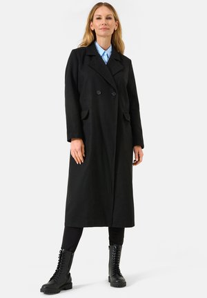 Black double-breasted coat with notched lapels, side pockets, and a relaxed fit, paired with black lace-up combat boots.