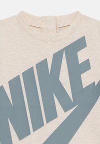 Béžová tkanina s velkým šedým logem Nike potisknutým diagonálně přes povrch.