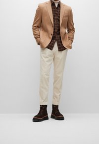 Bruine wolblenden blazer, geruite bruin en zwarte shirt, crème tapered broek, donkere veterschoenen van leer met een textuur en rubberen zolen.