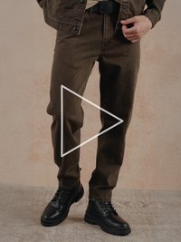 Hnědé bavlněné kalhoty s nohavicemi rovného střihu, doplněné černými koženými kotníkovými botami se šněrováním a strukturovanou podrážkou.