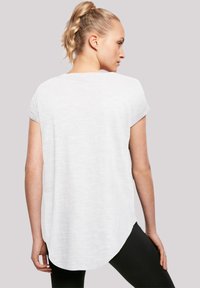 White, short-sleeve top with a curved hem and subtle texture, paired with black leggings, shown from the back against a neutral background.