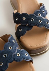 Paire de sandales beige avec des semelles épaisses en bois et des brides en suède bleu foncé festonnées avec des œillets métalliques.