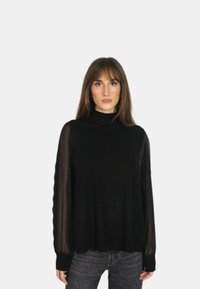 Top nero con maniche lunghe trasparenti, scollatura alta e una vestibilità rilassata. Presenta un corpo texturizzato e un contrasto di maniche lisce.