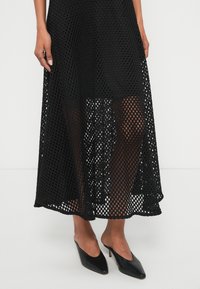 Čierna sieťovaná sukňa so šesťuholníkovým vzorom, polopriesvitným dizajnom a ležérnym lemom. Kombinovaná s čiernymi mulemi so špicatou špičkou.