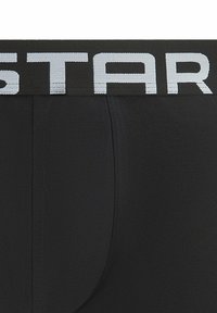Nahaufnahme von schwarzer Herrenunterwäsche mit breitem Bund, der große weiße Buchstaben "STAR" auf schwarzem Hintergrund zeigt.