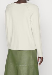 Vit ribbad långärmad topp i mjukt material med en böjd fåll, matchad med en grön läderkjol med glansig yta.