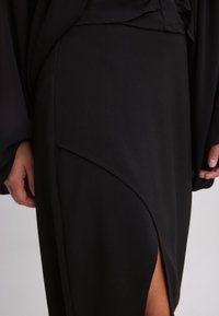 Falda negra con un diseño frontal asimétrico, hecha de una tela suave, con una abertura lateral y detalles de costura sutiles.