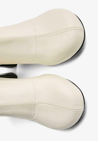 Botine din piele crem, cu o textură netedă, având detalii cusute și o talpă exterioară solidă de culoare neagră. Design minimalist, cu vârful rotunjit.