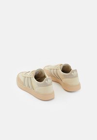 Beige Sneakers aus strukturiertem Wildleder, drei dunkle Streifen, Gummisohle und ein Logo-Patch an der Ferse. Schnür-Design mit einer runden Zehenform.