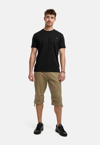 T-shirt noir à manches courtes avec une poche poitrine, associé à un short cargo beige clair avec desOurlets roulés. Porte des baskets noires.