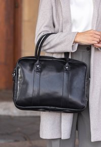 Sort læder laptop taske med to top-håndtag, der har en glat tekstur, diskret syninger og en lynlåslukning. Aksenteret med sølvfarvet hardware.