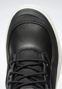Black sneaker featuring a textured synthetic upper with smooth leather accents, round toe, and white rubber sole, detailed with black laces.