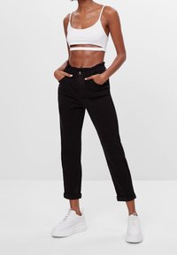 Pantalones negros de cintura alta con un cinturón fruncido, bolsillos frontales, combinados con una camiseta corta blanca y zapatillas blancas gruesas.