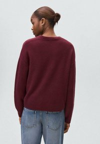 Burgundska jopica s sproščenim krojem, rebrastim ovratnikom in dolgimi rokavi, v kombinaciji s svetlobluzimi hlačami z visokim pasom. Gladka tekstura.