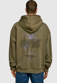 Hoodie surdimensionné vert olive avec une capuche, affichant un graphique de papillon et un texte stylisé au dos. Matière en coton douce et texturée.