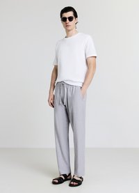 Weißes T-Shirt mit Struktur, graue Hosen mit Kordelzug und zwei Taschen sowie schwarze Sandalen. Einfaches, locker geschnittenes Design für mehr Komfort.