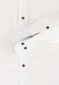 Weißes Hemd aus strukturiertem Stoff mit kontrastierenden dunkelblauen Knöpfen und Doppelmanschetten. Enthält eine Tasche und sorgfältige Nähte.