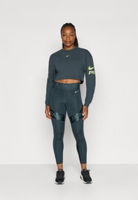 Mørkegrå cropped sweatshirt og matchende leggings med shiny "PR" logo, parret med sorte træningssko. Glat, strækbart stof.