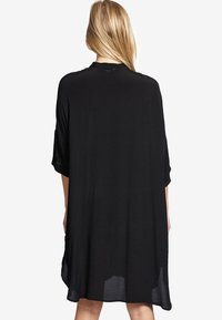 Svart, löst sittande klänning med korta, vida ärmar och rundad halsringning. Lättviktig tyg med mjuk textur som slutar ovanför knäna.