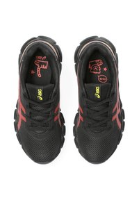 Baskets de sport noires avec des accents rouges, tige en mesh, bout rond, col rembourré et semelle extérieure à motif distinctif. Logo de la marque visible.