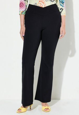 Black, fitted pants with a wide waistband, featuring a smooth texture and flared legs. Paired with yellow knotted sandals.