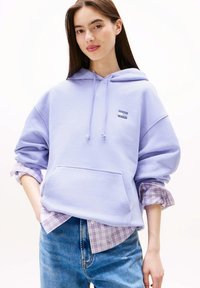 Lavendelkleurige hoodie met voorklep en trekkoorden, gecombineerd met een geruit overhemd eronder. Losse pasvorm; gemaakt van een katoenmengsel.