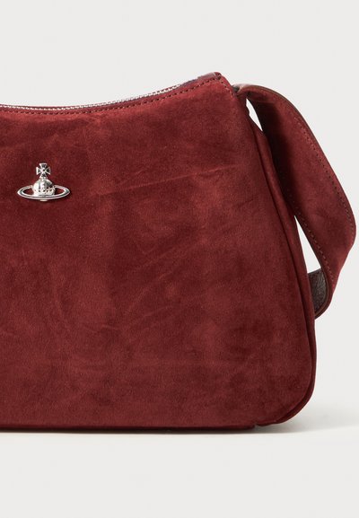 Bolsa de mão em camurça vermelha profunda com logotipo em forma de órbita prateada, fecho com zíper no topo e alça larga sobre fundo branco.