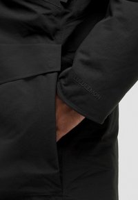 Zwarte outerwear heeft een gladde stoftextuur, een gestructureerd ontwerp en een prominent Lululemon-logo op de manchetten.