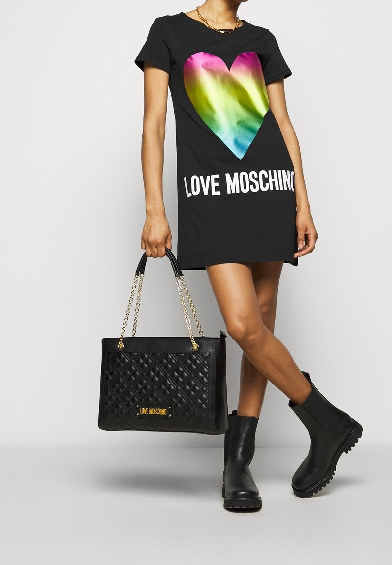 Černé tričkové šaty s barevným srdcovým graphic, s nápisem "LOVE MOSCHINO" tučně bílými písmeny; doplněné černou prošívanou kabelkou a černými botami.