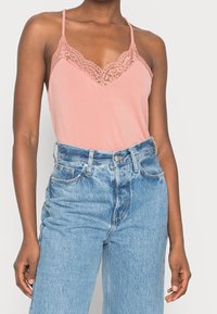 Persikofärgad linne med spetsdetaljer, justerbara axelband och mjuk känsla, tillsammans med högmidjade ljusblå jeans.