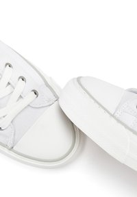 Weiße Leinwand-Sneaker mit weißen Gummisohlen, die Metallösen und flache weiße Schnürsenkel aufweisen. Einfaches Design mit glatter Textur.