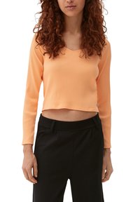 Geribbelde, cropped lange mouw top in een zachte perzikkleur met een ronde hals, gecombineerd met zwarte high-waisted broeken.