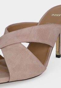 Mule-sandale beige en daim à talon haut avec larges brides superposées et talon stiletto fin avec détail logo doré.