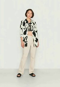 Camisa preta e branca com padrão abstracto por cima de uma t-shirt cropped preta, combinada com calças bege e sandálias pretas. A camisa tem um corte largo e mangas até aos três quartos.