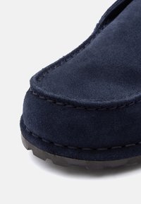 Κοντινή λήψη της μύτης ενός παπουτσιού από σουέτ σε σκούρο μπλε χρώμα με ορατή ραφή και μαύρη καουτσούκ σόλα σε λευκό φόντο.