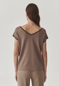 Haut marron à col en V avec des manches courtes, orné de bordures bleu marine autour de l'encolure. Texture lisse, coupe décontractée, associé à un pantalon beige assorti.
