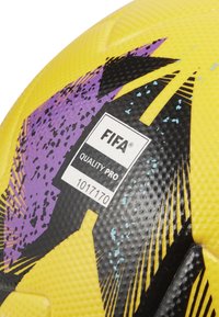 FIFA Quality Pro futbolo kamuolys su tekstūruota geltona danga, puošiamas purpuriniais ir juodais abstrakčiais raštais bei kokybės etikete.