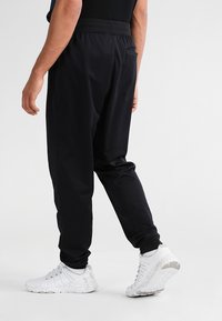 Svarta träningsbyxor med avslappnad passform, elastisk midja, sidofickor, tillverkade av ett mjukt och lätt material, i kombination med vita sneakers.