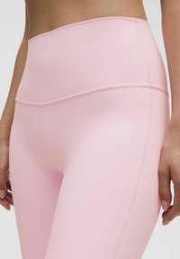 High-waisted pink leggings made of smooth, stretchy fabric with a clean, seamless design and stitched accents along the sides.