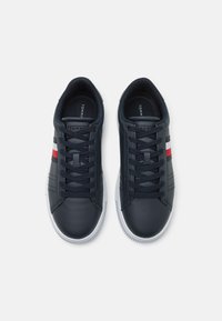 Sneakers in pelle blu con suole in gomma bianche, caratterizzate da dettagli a strisce rosse e bianche. I lacci e le cuciture sono anch'essi di un blu scuro.