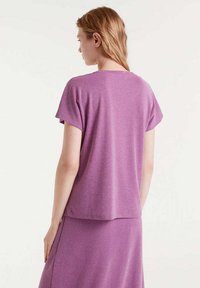 Top corto morado con mangas cortas, textura suave y un corte relajado, combinado con una falda morada a juego. Vista desde la parte de atrás.