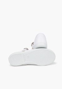Tenisi albi din pânză cu vârf rotunjit, talpă din cauciuc alb texturat și accente decorative sub formă de curele. Partea inferioară are un model de profil pentru aderență.