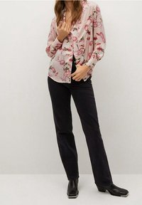 Chemise boutonnée rose clair à motifs floraux, associée à un jean noir à jambes droites et des bottines noires à talons blocs.