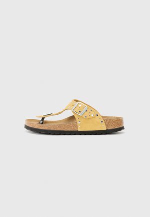 Sandali flip-flop in suede giallo con dettagli neri, cinturino con fibbia e decorazioni a borchie. Suola in sughero e fondo in gomma nera testurizzata.