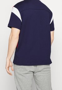 Navy blue short-sleeve T-shirt with white and red accents on sleeves. Soft cotton material with a straight hem and relaxed fit.