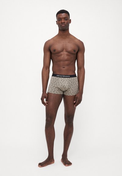 Boxer briefs in beige with all-over black logo pattern, featuring a black elastic waistband with "Emporio Armani" branding. Made from smooth fabric.