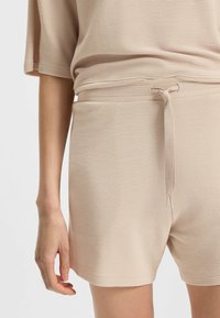 Beige geribde shorts met een trekkoord in de taille, een gladde textuur en een lichte glans, gecombineerd met een bijpassende losse top.