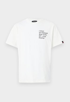 Witte katoenen t-shirt met zwarte tekst aan de voorkant: "Ik zal worden vrijgelaten New York, NY - Juli, Replay," met korte mouwen en een ronde halslijn.