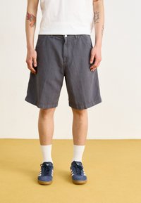 Grå bomullsshortser med løs passform, knappelukking og sidelommer, kombinert med marineblå skinnskotter og hvite crew-sokker.