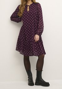 Lila klänning med prickar, rynkad nederkant och nyckelhålsutskärning, matchad med svarta ankelstövlar. Transparent tyg ger en lätt textur.